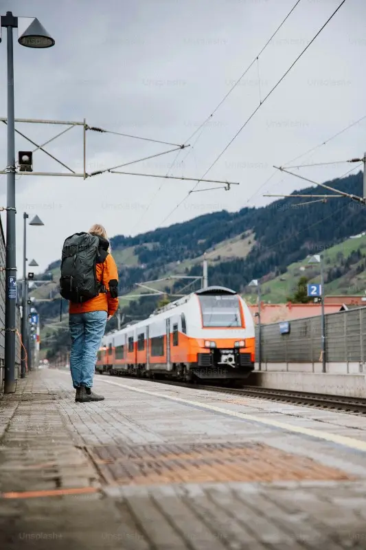 A traveller with a backpack watching a passenger train pull into a mountain station