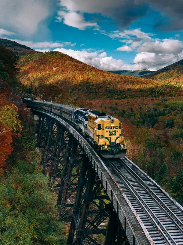 A yellow freight locomotive crossing a viaduct through autumn hills
