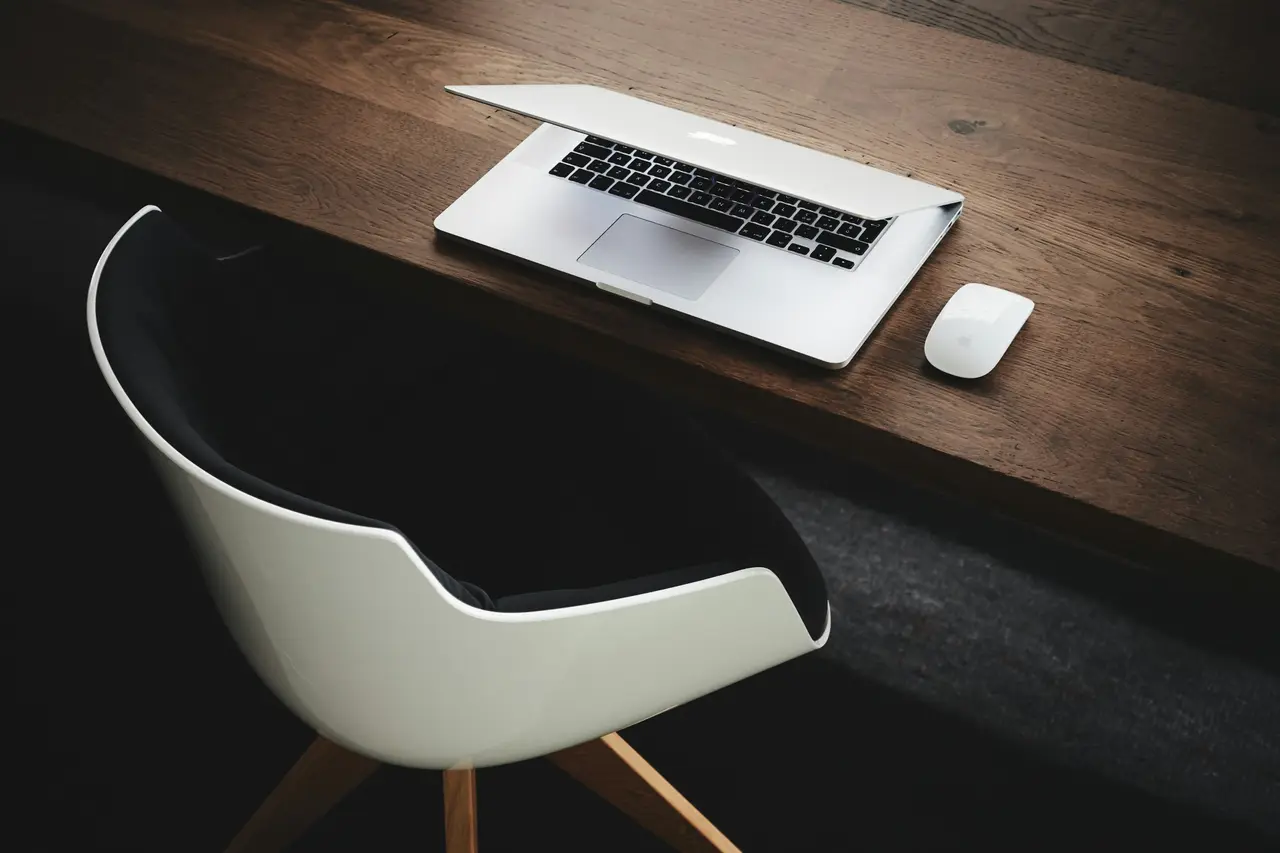 A laptop on a desk beside a white chair