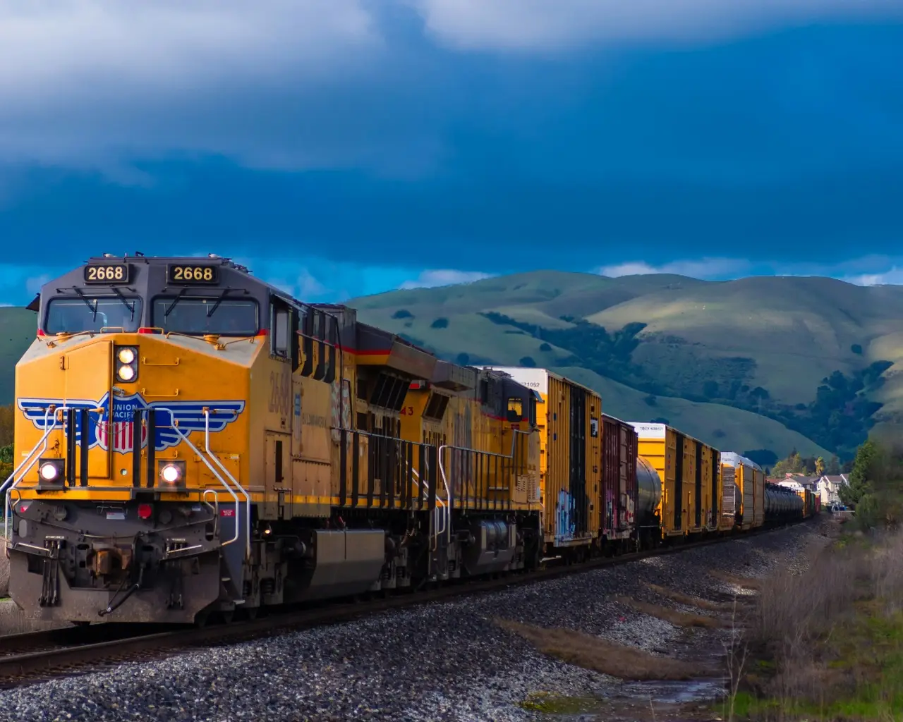 A yellow freight locomotive hauling wagons through mountains