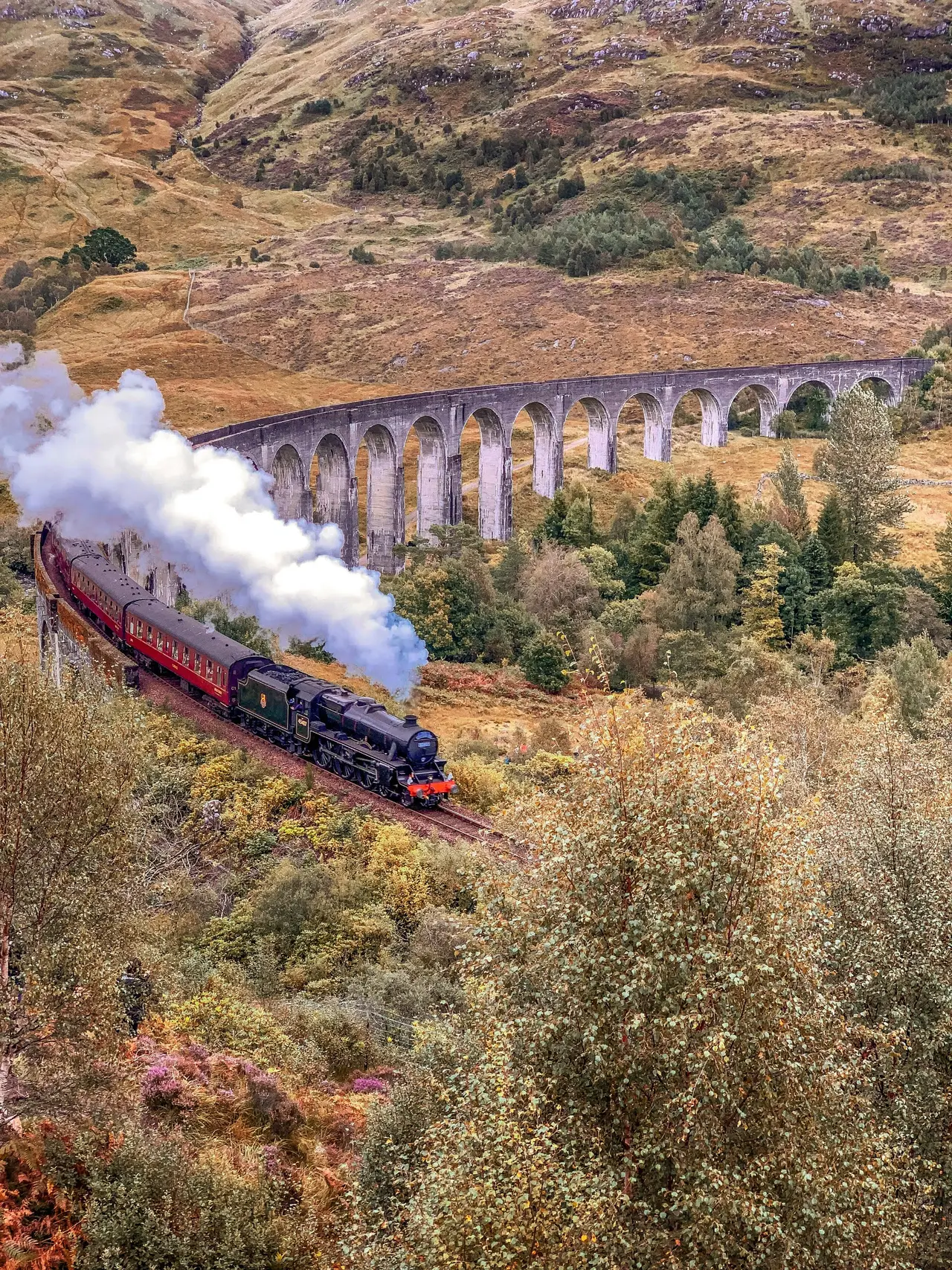 A steam locomotive crossing a stone viaduct